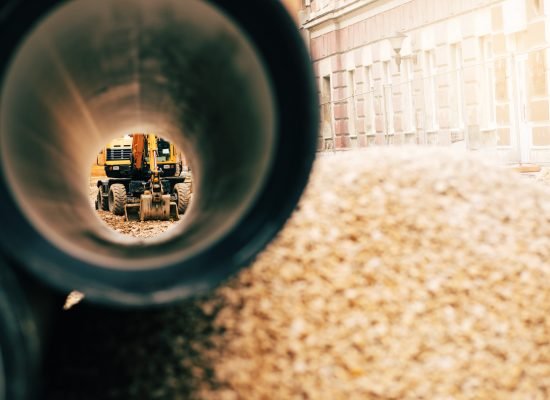 A dynamic view of a construction site showing an excavator through the opening of a large pipe, emphasizing industry and progress.